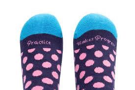 Pink dotty and blue socks with Practice Makes Progress written at the toe